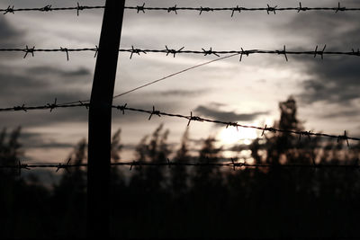 Low angle view of silhouette barbed wire fence against sky