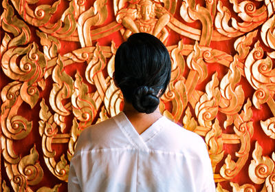 Rear view of young woman with hair bun standing against wall
