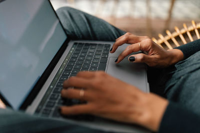 Side view of crop faceless ethnic female entrepreneur sitting in chair at home and working on online project while using netbook