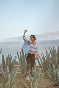 Full length of woman with hand raised standing on land against sky