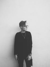 Young man wearing eyeglasses standing against wall