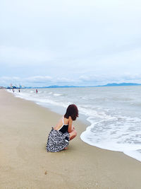 Rear view of woman standing at beach against sky