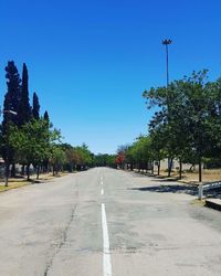 Road amidst trees against clear blue sky