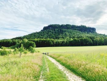 Dirt road amidst field against sky