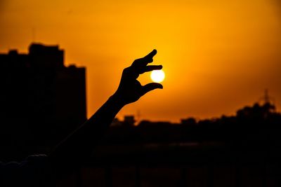 Optical illusion of silhouette person holding sun during sunset