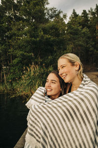Smiling young female friends wrapped in towel during vacation