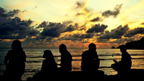 Silhouette of people on beach against cloudy sky