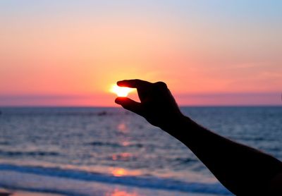 Cropped image of silhouette person holding sea during sunset