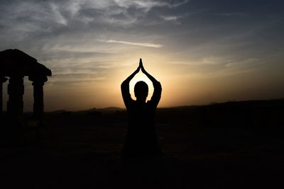 Silhouette woman with hands clasped meditating against sky during sunset