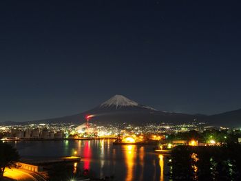 Illuminated city by mountains against clear sky at night