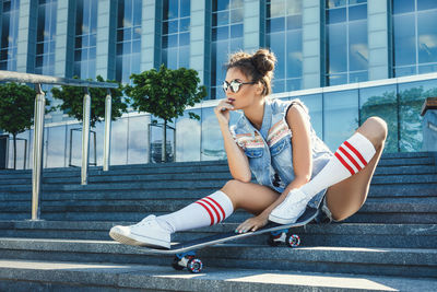 Full length of woman with skateboard sitting on steps outdoors