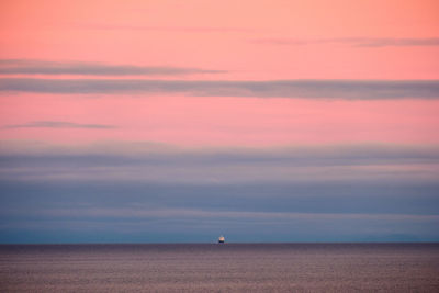 Scenic view of sea with ship in the distance against sky during sunset