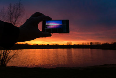 Man photographing sunset over lake through smart phone