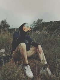 Man sitting on field against sky