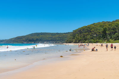 Group of people on beach against clear blue sky