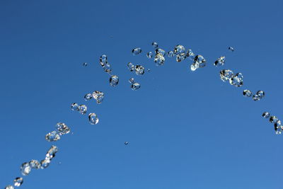 Low angle view of bubbles against clear blue sky