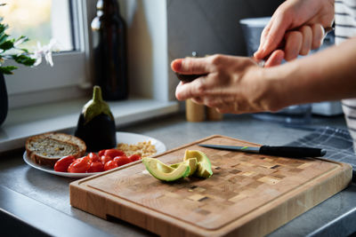 Woman cutting avocado on cutting board to prepare breakfast