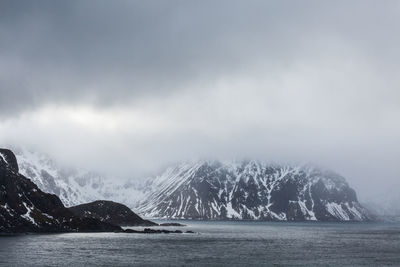 Scenic view of sea by snowcapped mountains against sky