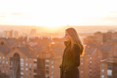 Young woman looking away against cityscape and sky