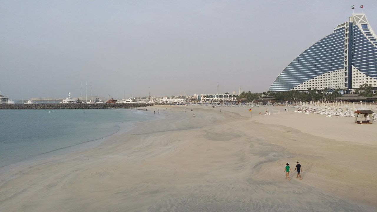 beach, water, sea, sand, leisure activity, shore, built structure, lifestyles, large group of people, architecture, men, vacations, tourist, tourism, sky, copy space, clear sky, mixed age range, travel destinations