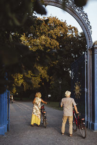 Rear view of heterosexual couple wheeling cycle in park during vacation