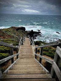 Rear view of man walking on pier on sea against sky