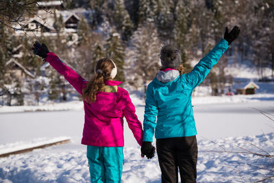 Woman by daughter with arms raised in snow during winter