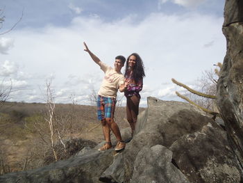 Full length of man and woman standing on rock in forest against sky