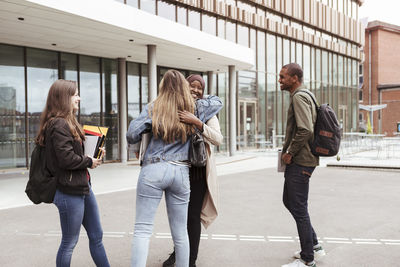 Multi-ethnic friends greeting while standing at high school campus