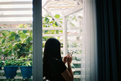 Woman using mobile phone at window