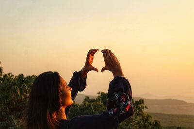 Portrait of woman with arms raised against sky during sunset