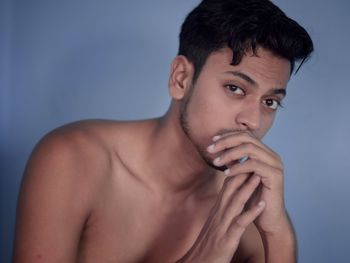 Portrait of shirtless young man against blue background