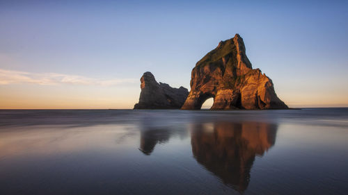 Rock formation in sea against sky during sunset
