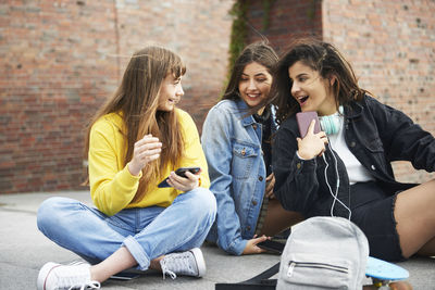 Young friends using phone while sitting on street