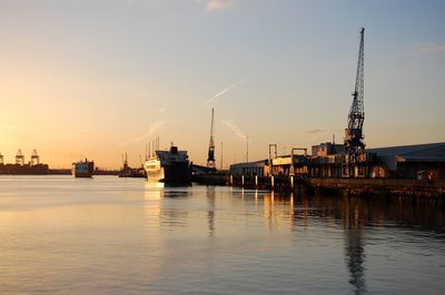 Silhouette cranes at harbor against sky during sunset