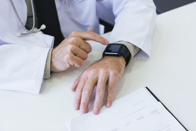 Cropped image of doctor using smart watch at table in hospital