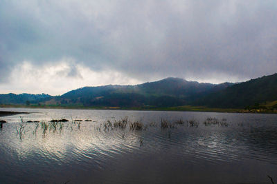 Scenic view of lake and mountains against cloudy sky