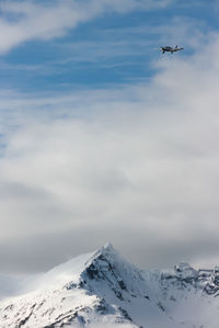 Low angle view of airplane flying over snowcapped mountains against sky