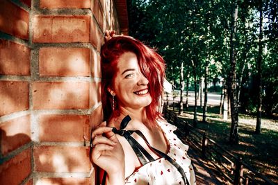 Portrait of smiling young woman against brick wall