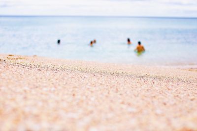 Defocused image of people swimming on beach against sky