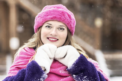 A  woman in a pink scarf and hat, white mittens and a purple fur coat outdoors in a park in winter