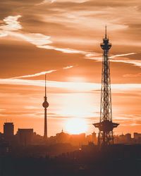 Silhouette of communications tower in city during sunset