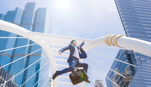 Low angle view of businessman jumping against buildings in city