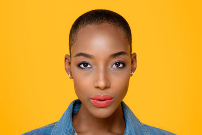 Close-up portrait of serious young woman over yellow background