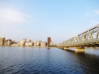 Bridge over river by buildings against sky in city