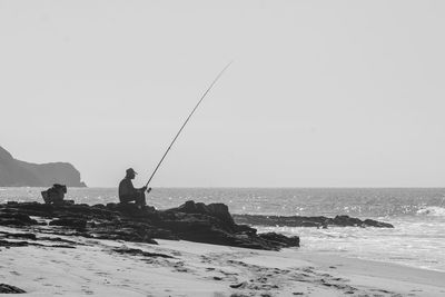 Fishing rod on rock by sea against clear sky