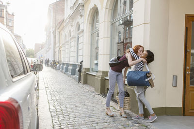 Mother kissing daughter on sidewalk against building in city