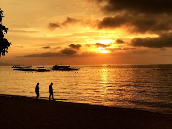 Silhouette people on beach against sky during sunset