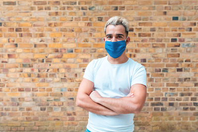 Portrait of man wearing mask standing against brick wall