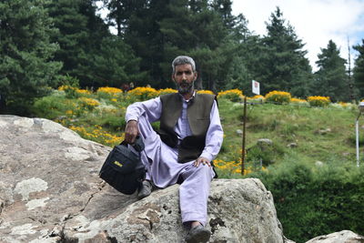 Portrait of young man sitting against trees